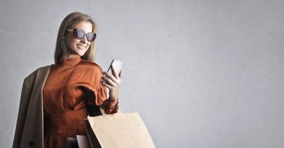 Laptop Stand - Smiling female in trendy wear and stylish sunglasses standing with paper shopping bags on background of gray wall and browsing mobile phone