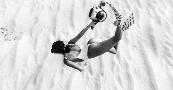 Underwater Cameras - Black and white faceless slim female wearing swimsuit and flippers snorkeling above sandy sea bottom in transparent waters and carrying camera in waterproof cover
