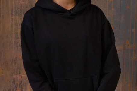 Wearable Cameras - Glad young African American female with Afro hairstyle wearing black hoodie and pants standing against shabby wooden wall and looking at camera