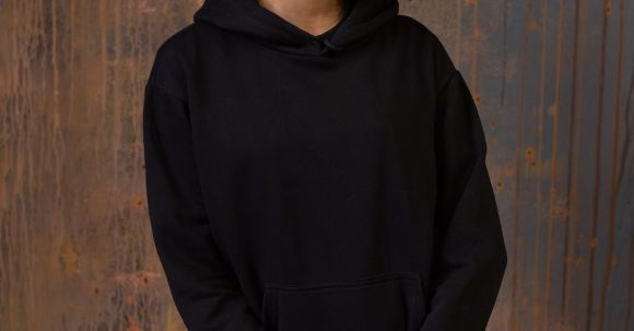Wearable Cameras - Glad young African American female with Afro hairstyle wearing black hoodie and pants standing against shabby wooden wall and looking at camera