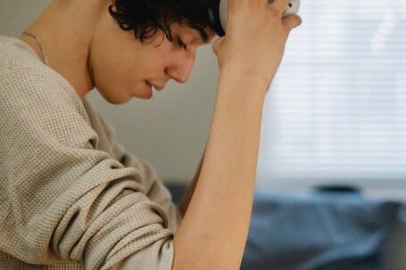 VR Accessories - Side view of young Hispanic male gamer sitting on bed and putting on VR headset on weekend day at home