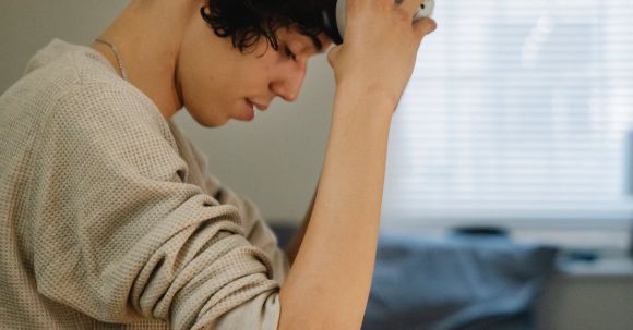 VR Accessories - Side view of young Hispanic male gamer sitting on bed and putting on VR headset on weekend day at home