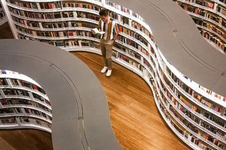 E-Readers - Man Standing Inside Library While Reading Book