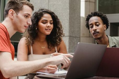 Remote Collaboration Apps - Group of diverse young male and female diverse colleagues discussing project details while working together on laptops in outdoors cafe