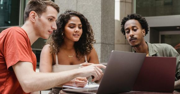 Remote Collaboration Apps - Group of diverse young male and female diverse colleagues discussing project details while working together on laptops in outdoors cafe