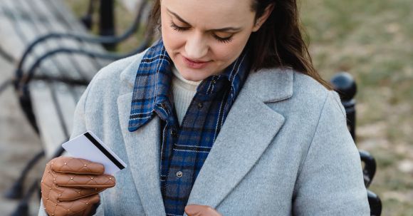 Mobile Payment Apps - Content young female in blue coat making online payment with smartphone while sitting on bench in park on early spring day