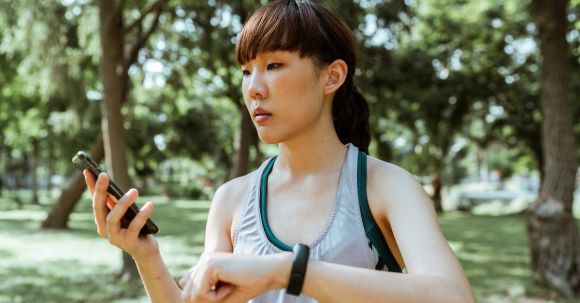 Wearable Sleep Monitors - Concentrated young Asian woman using smartphone in park