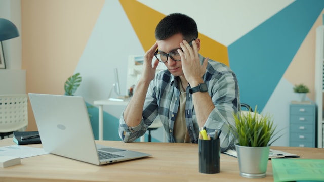 man-holding-head-in-frustration-at-desk-with-laptop